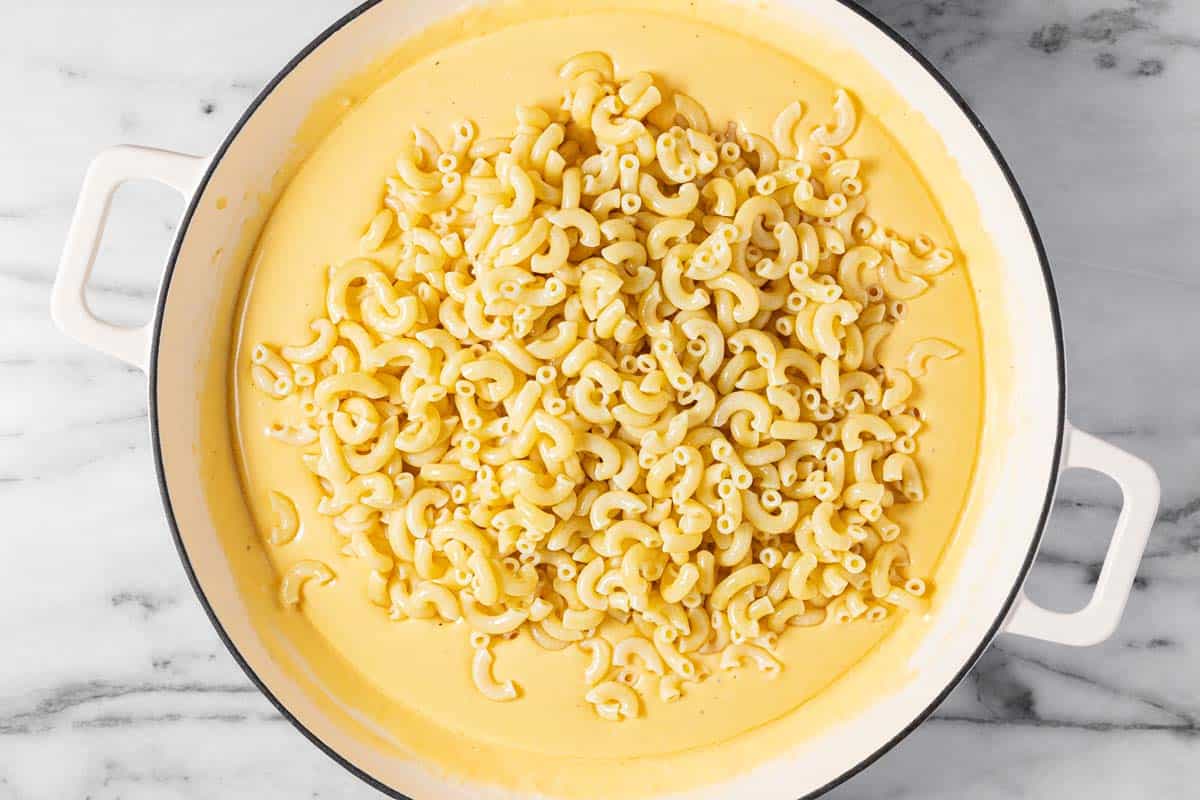 Al dente macaroni noodles added to a large pan of cheesy sauce. 