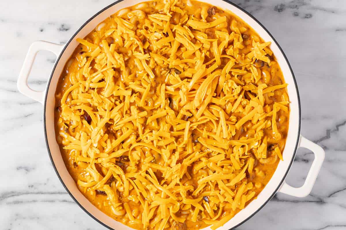 Large pan of chili mac topped with shredded cheddar cheese. 