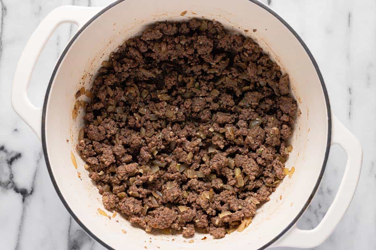 Large pot filled with diced onion, sauteed garlic, and browned ground beef. 