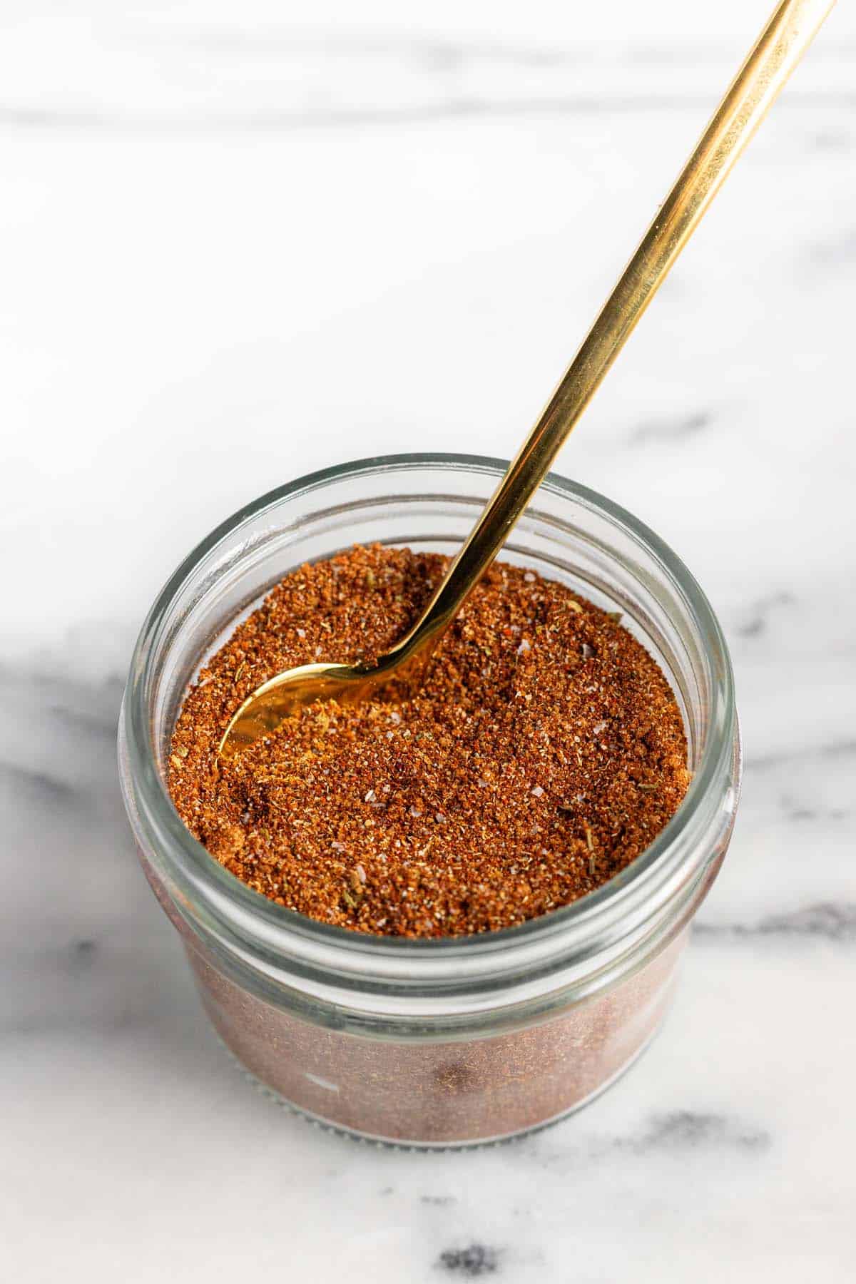 Small mason jar filled with homemade chili seasoning mix and a small spoon. 