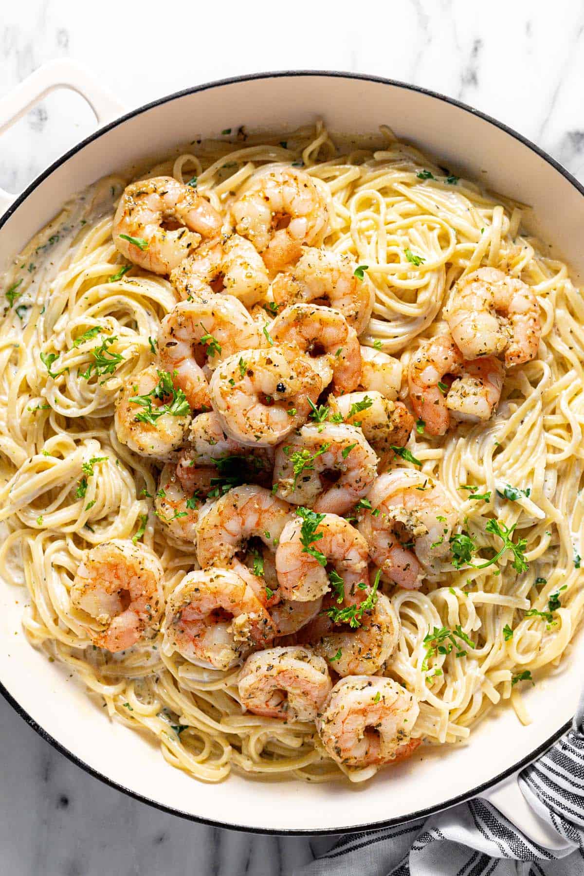 A large pan filled with creamy shrimp pasta garnished with parsley. 