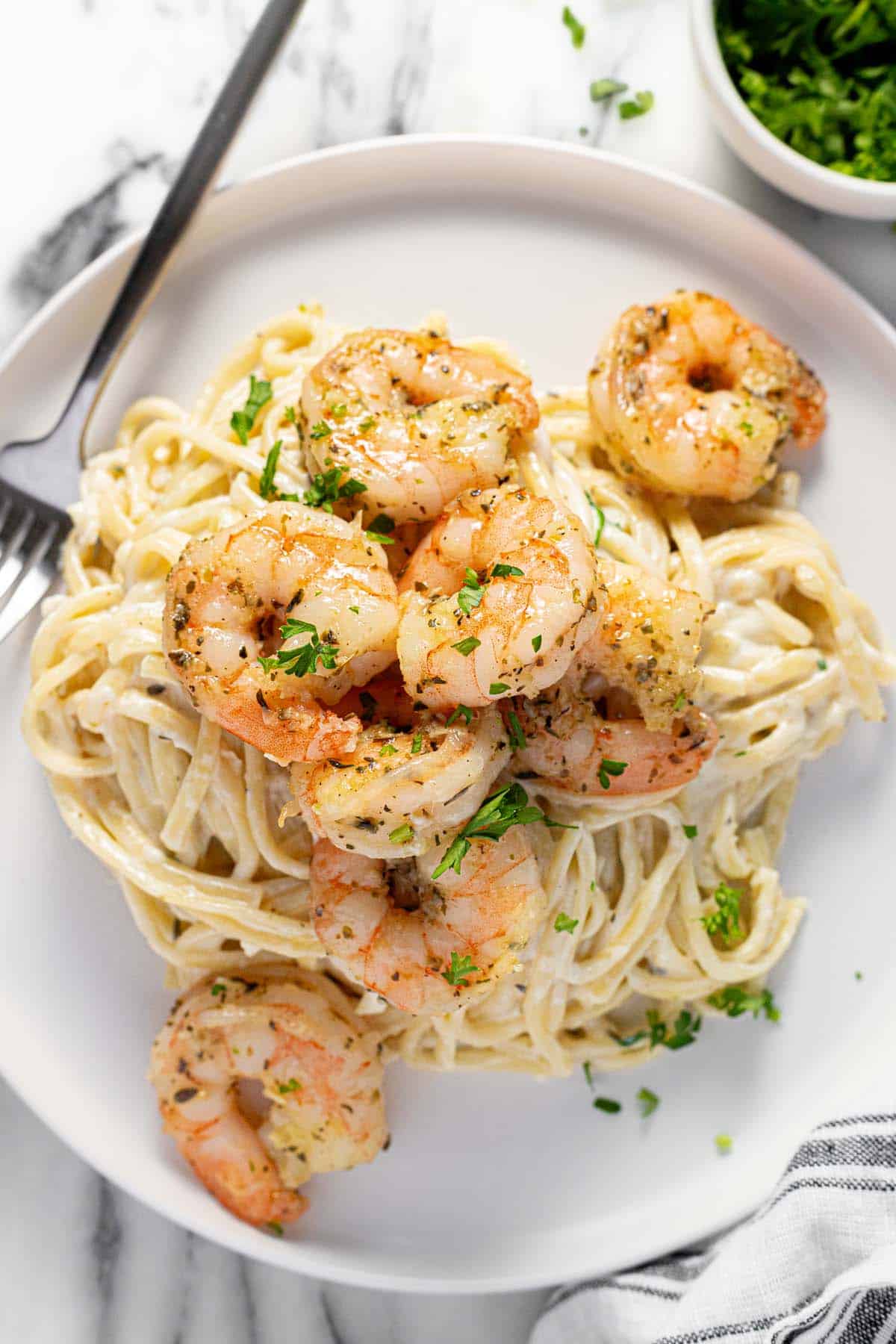 Plate with creamy linguine topped with garlic shrimp garnished with parsley. 