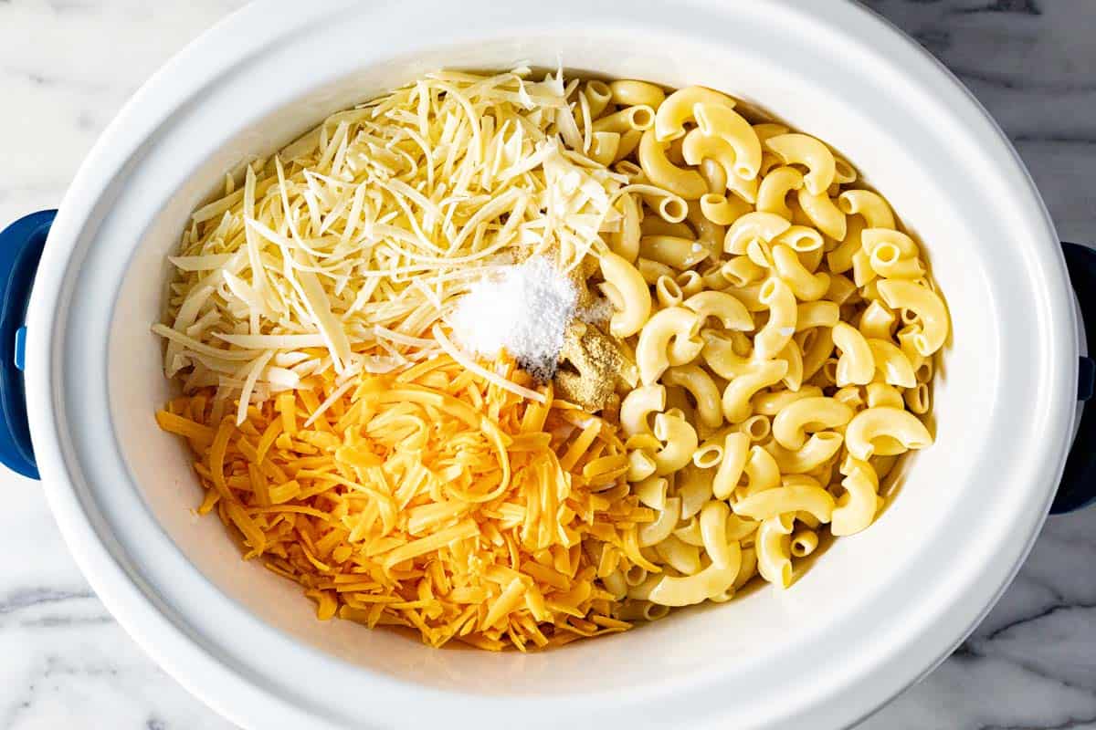 Large crock pot filled with elbow macaroni noodles, shredded cheese, evaporated milk, and half and half to make slow cooker mac and cheese. 
