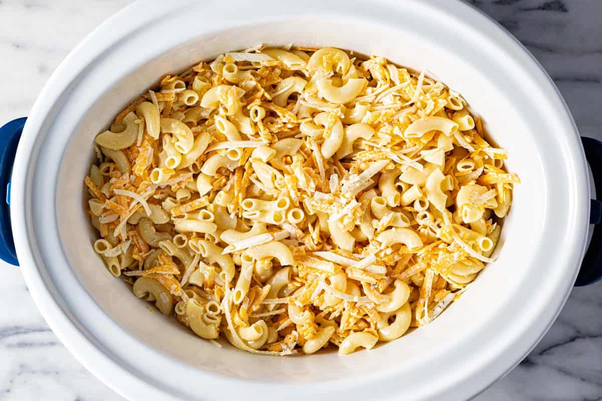 Large slow cooker insert filled with ingredients to make crock pot macaroni and cheese. 