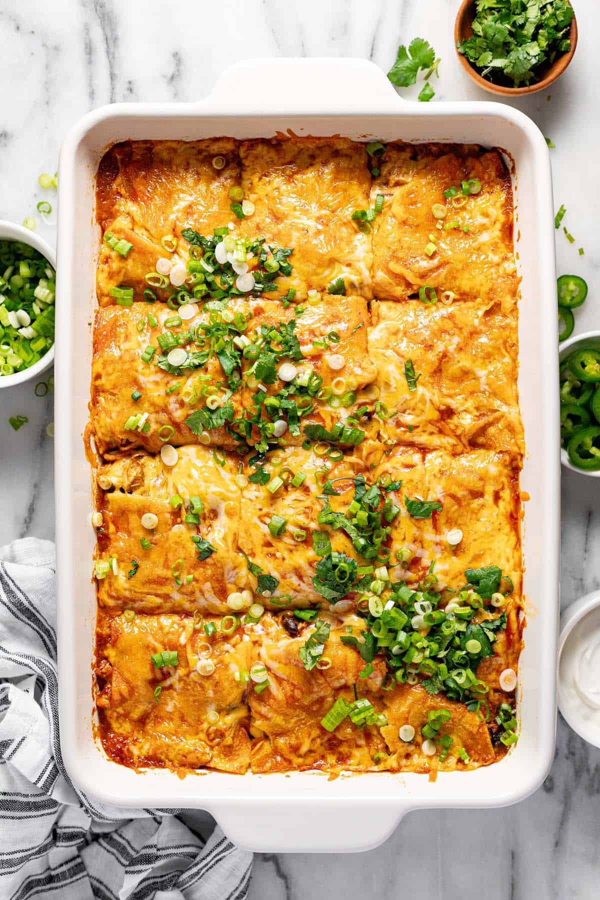 Large baking dish filled with cheesy chicken enchilada casserole garnished with sliced green onion. 
