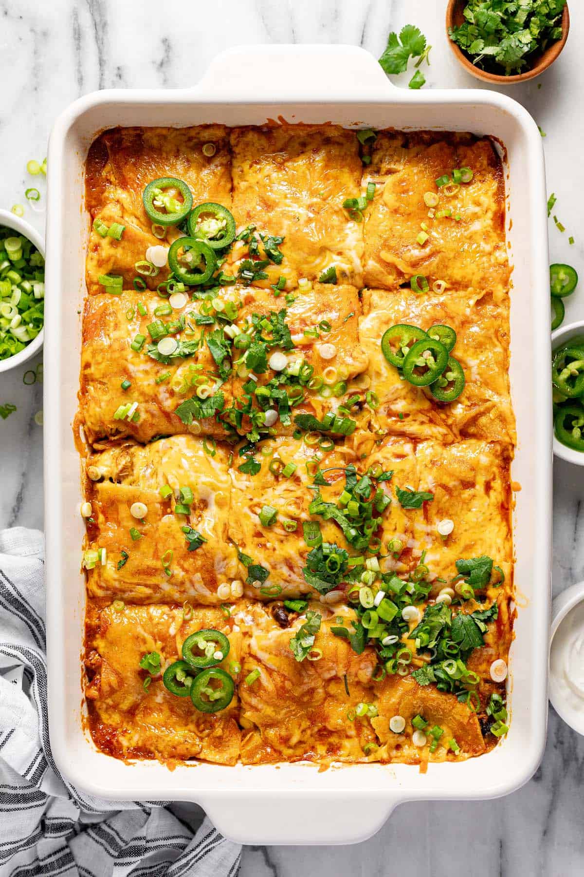 Large baking dish filled with cheesy chicken enchilada casserole garnished with sliced green onion. 