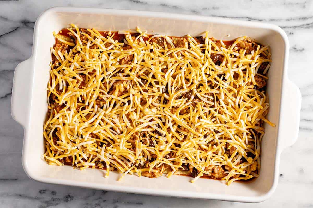 Ingredients layered in a large casserole dish to make chicken enchilada casserole. 