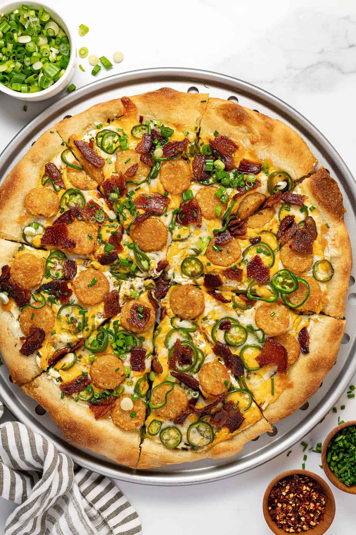 Jalapeno popper pizza on a round pizza pan garnished with chives. 