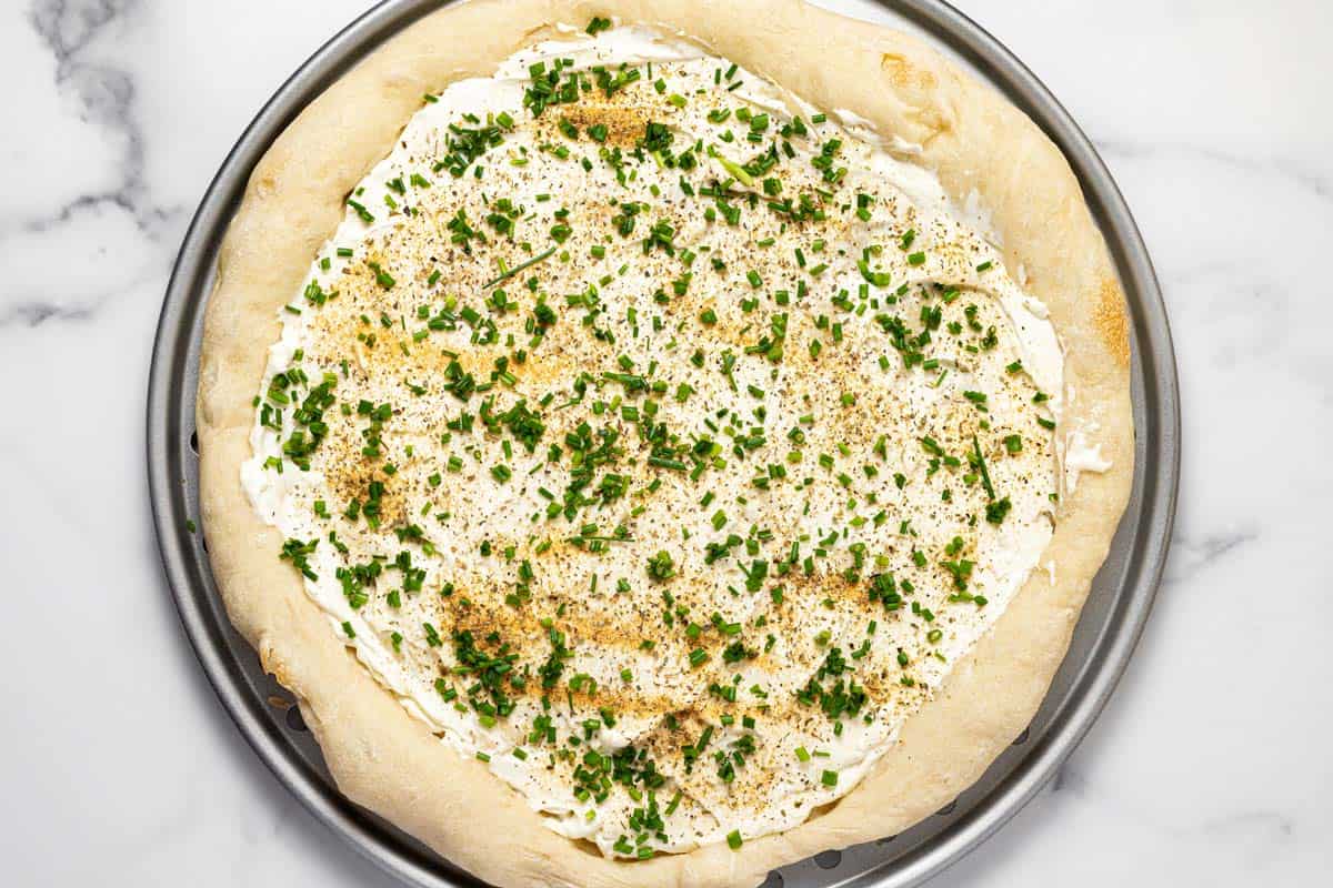 Partially baked pizza crust topped with cream cheese, spices, and chives. 