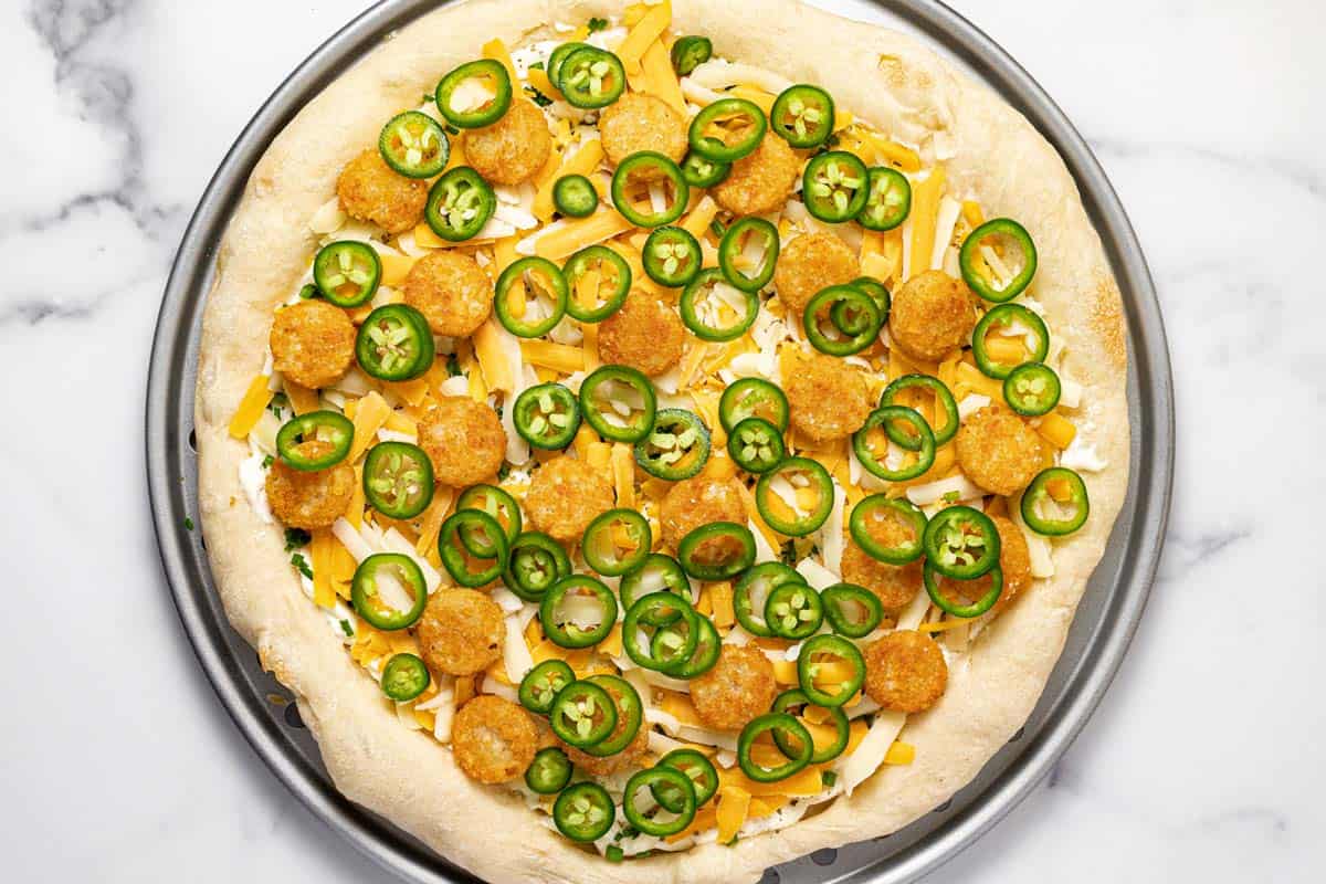 Pizza crust topped with cheese, tater tots, and sliced jalapenos. 