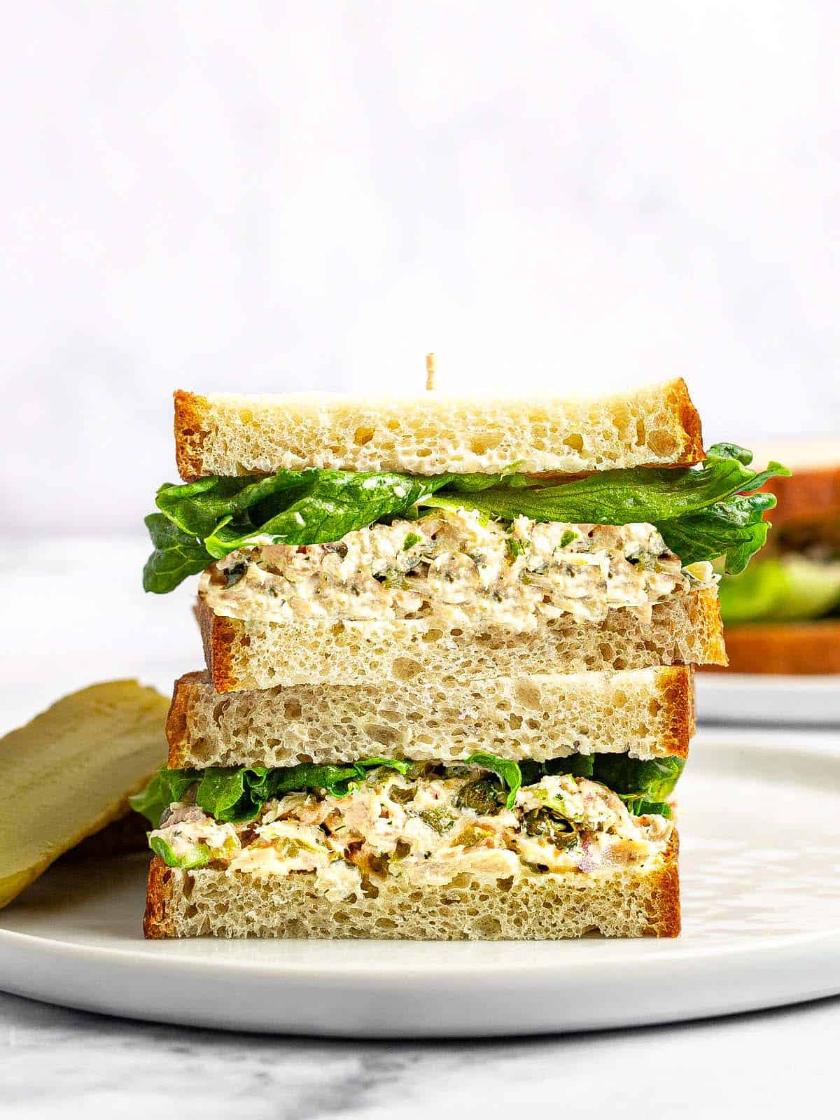 Tuna sandwich with lettuce sliced in half and stacked on a white plate.