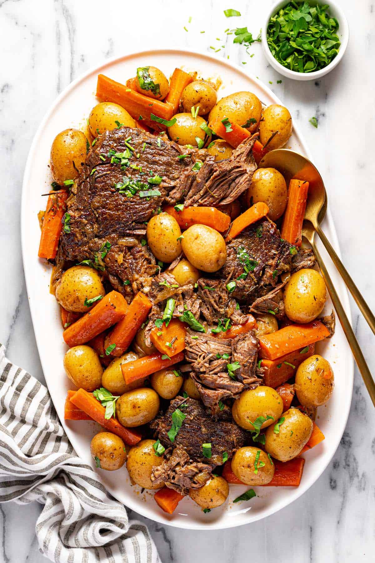 Large serving platter filled with shredded pot roast, carrots, and potatoes garnished with parsley. 