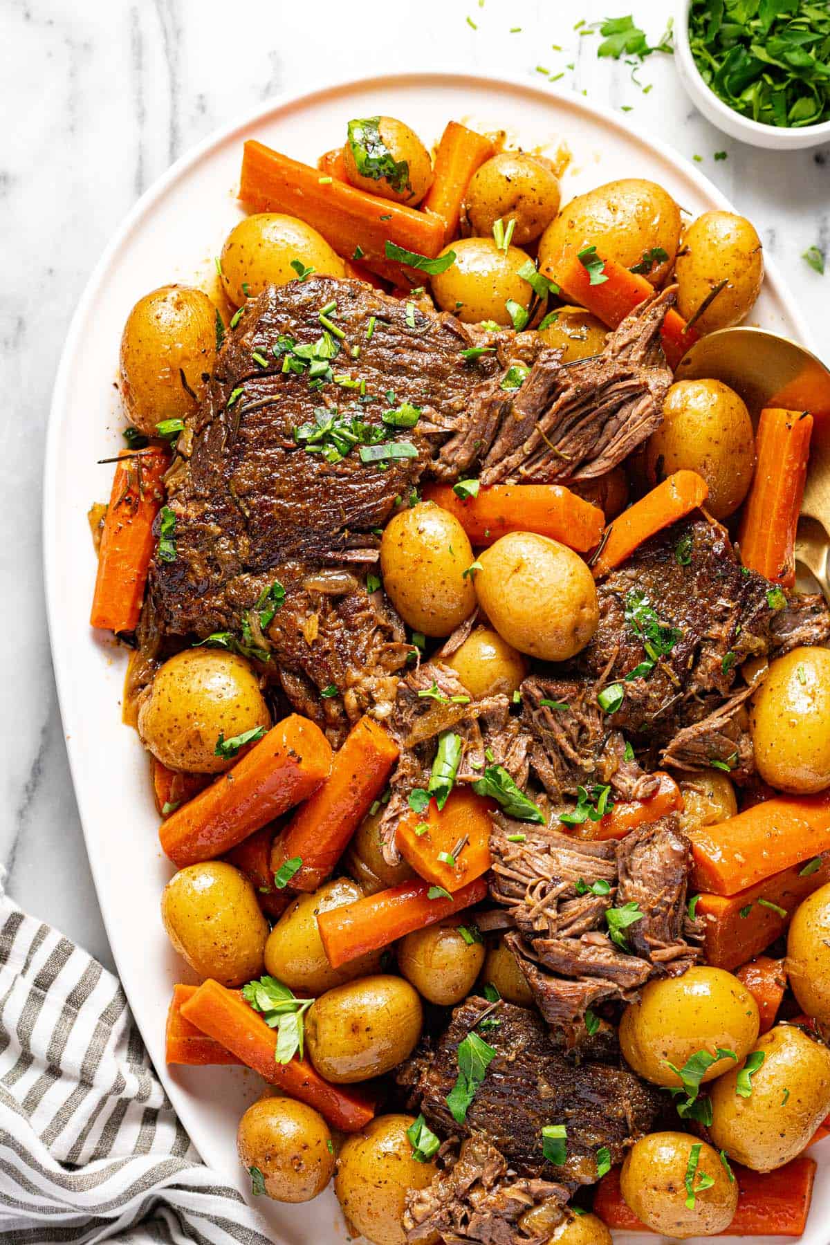 Large serving platter filled with shredded pot roast, carrots, and potatoes garnished with parsley. 