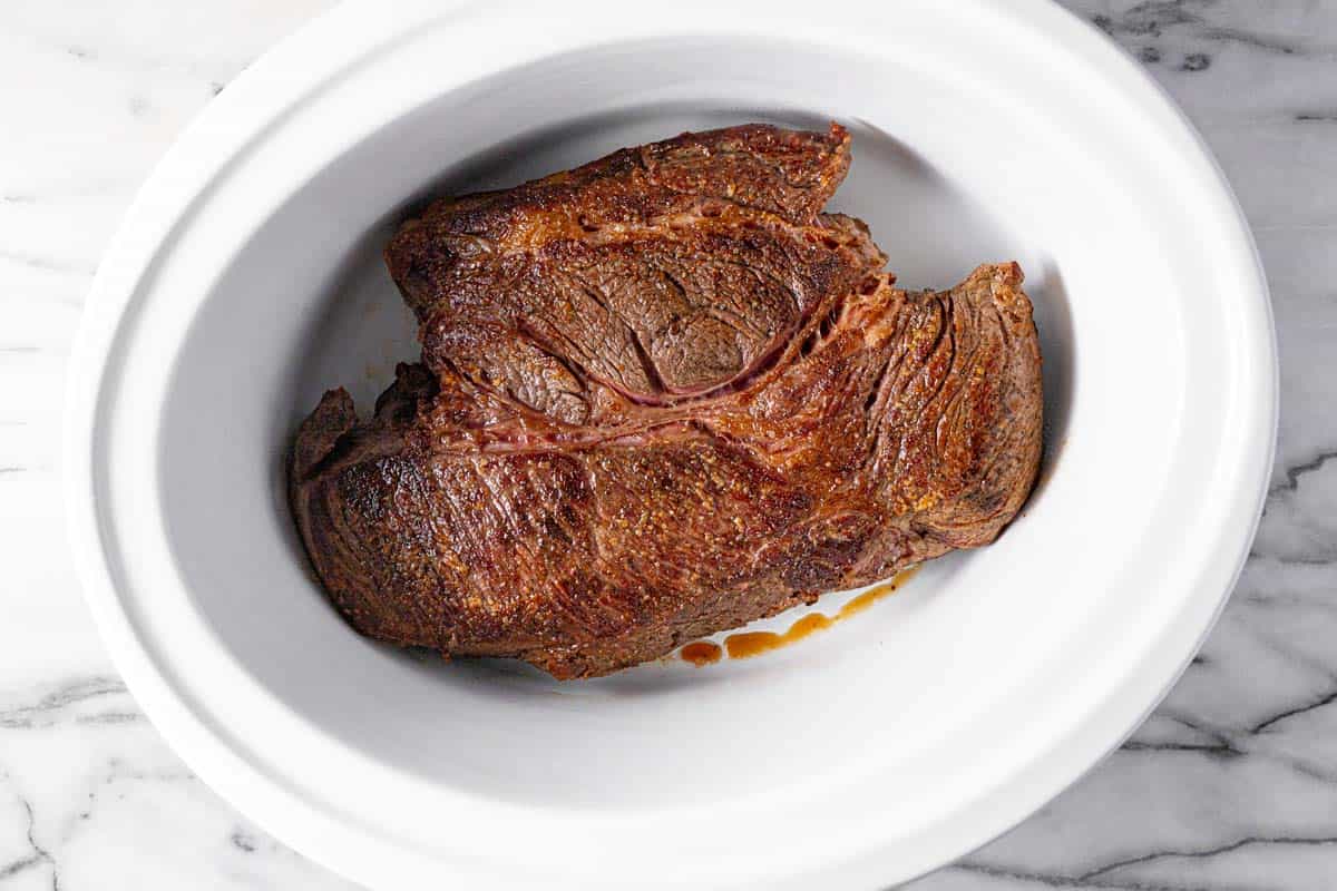 Large crock pot insert with a seared pot roast in it. 