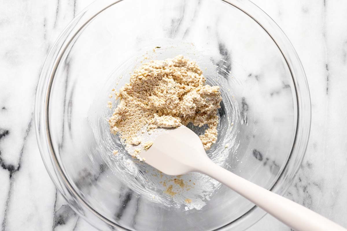 Bowl filled with breadcrumbs combined with heavy cream and a spatula. 