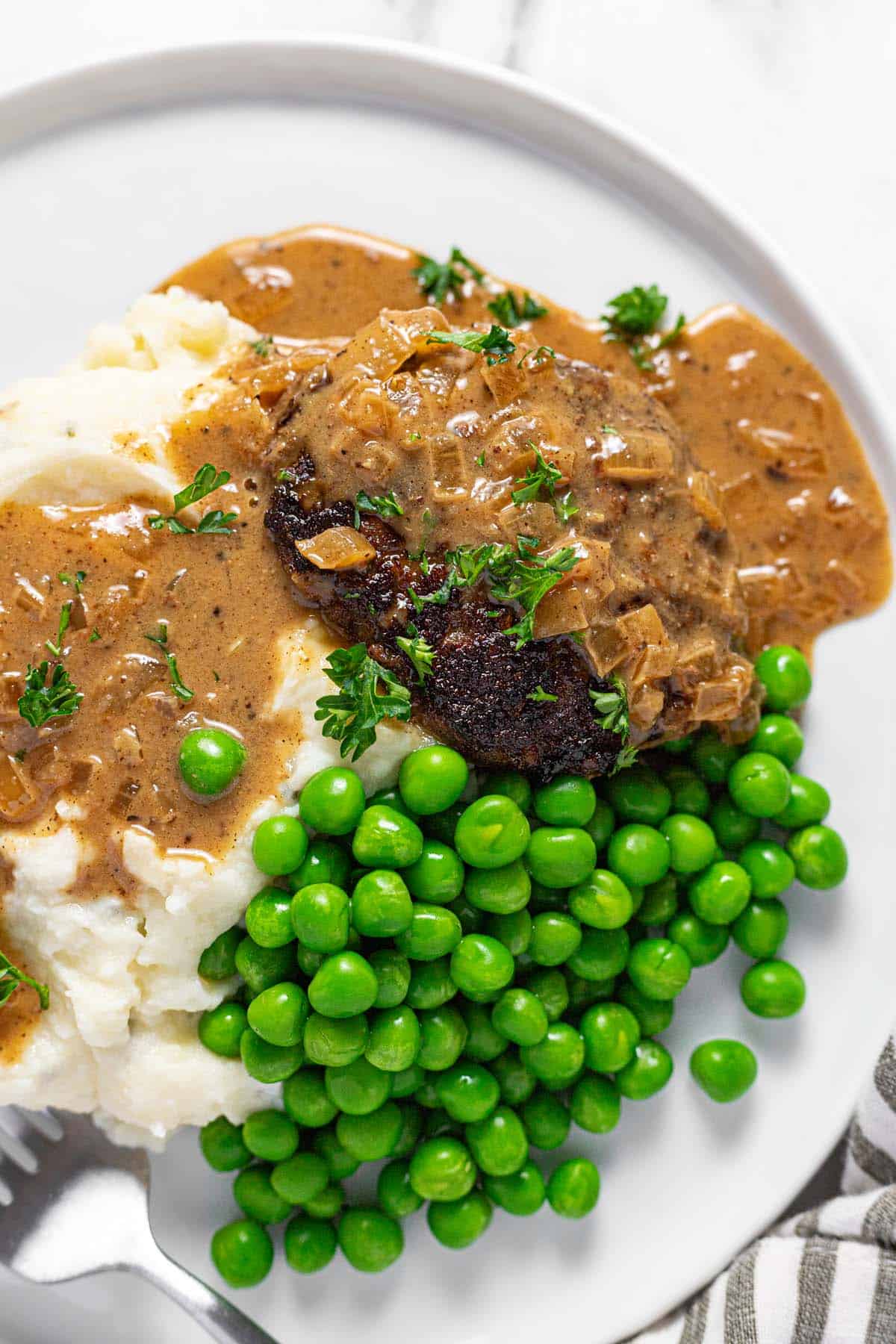 Large plate filled with mashed potatoes, peas, and a homemade hamburger steak topped with onion gravy. 