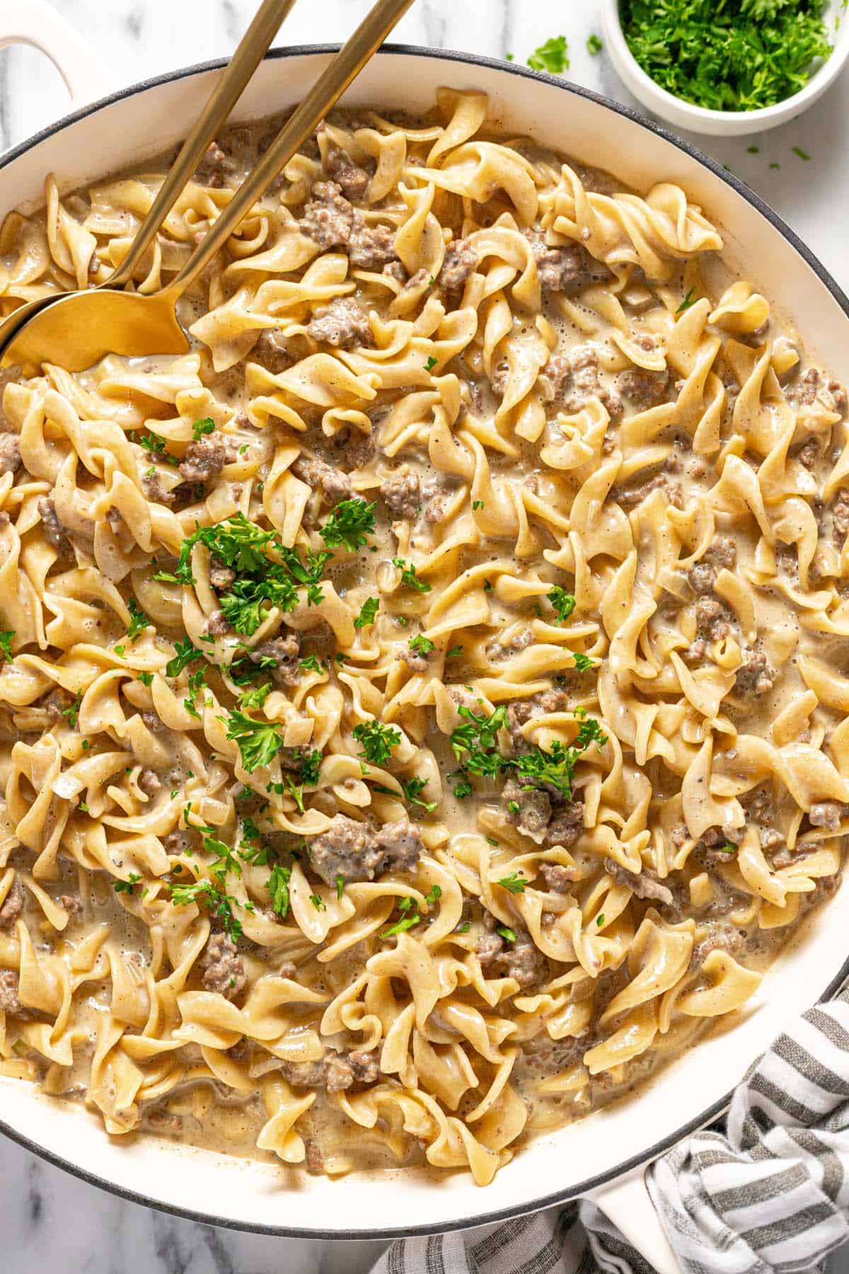 Large pan filled with creamy beef and noodles recipe garnished with parsley. 