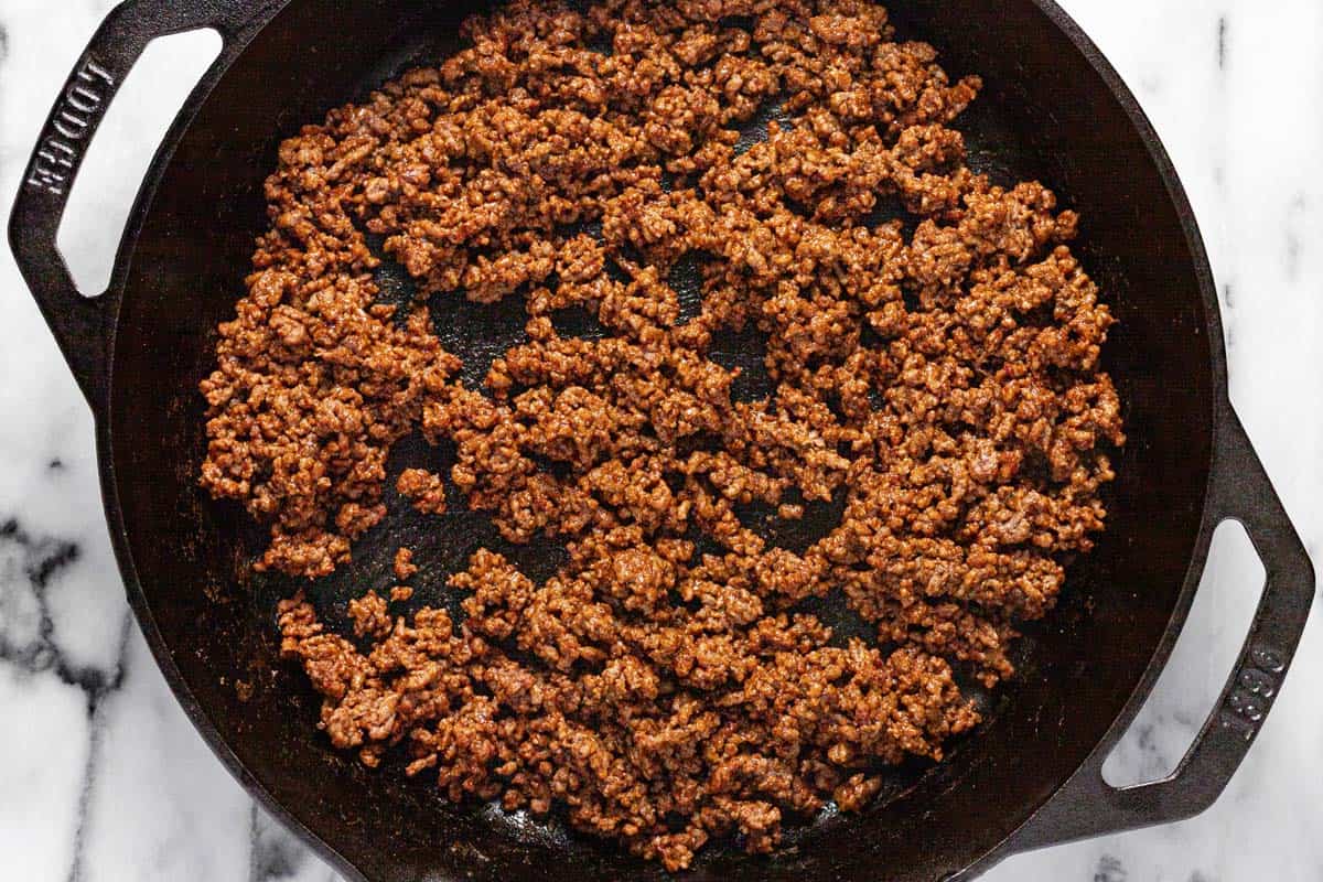 Cast iron skillet filled with browned ground beef seasoned with taco seasoning. 