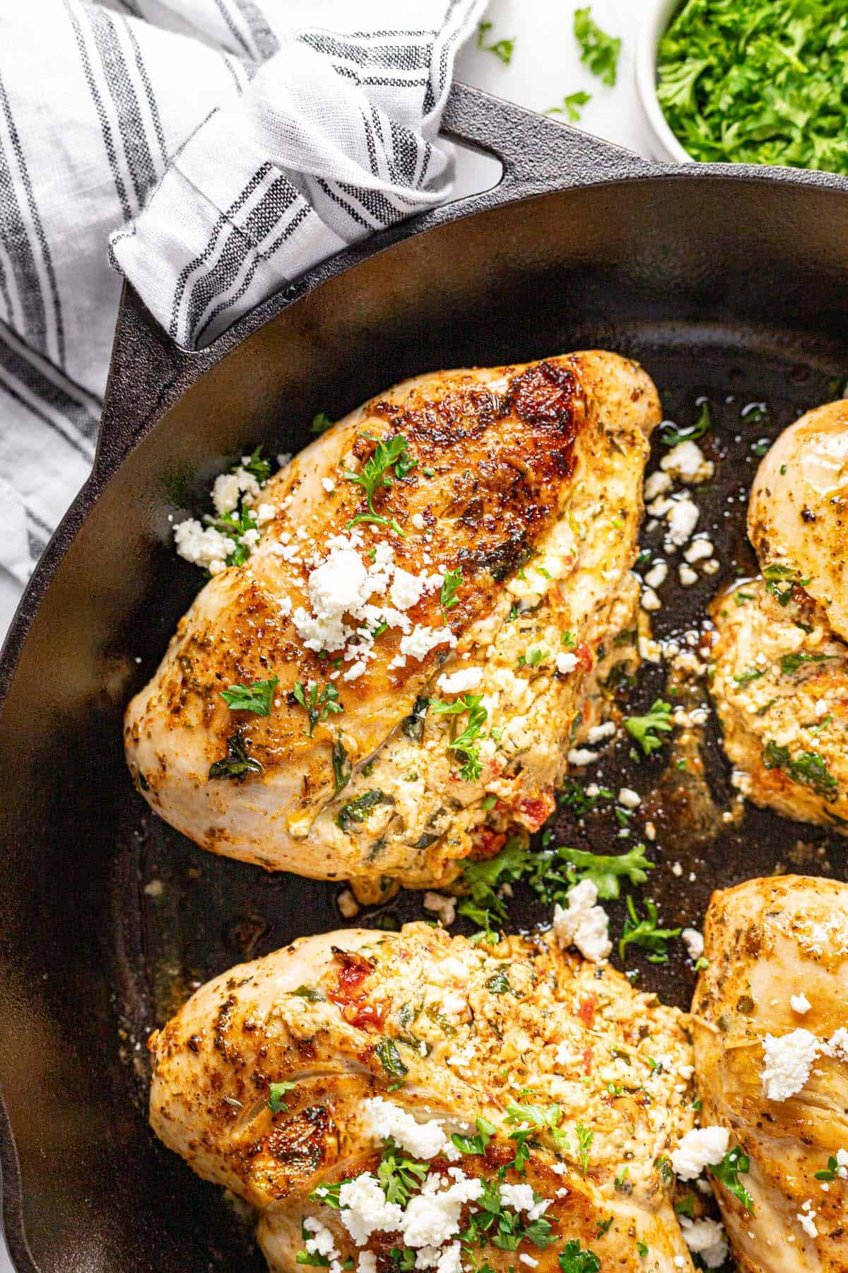 Close up of a cast iron skillet with stuffed chicken breasts topped with feta and parsley. 