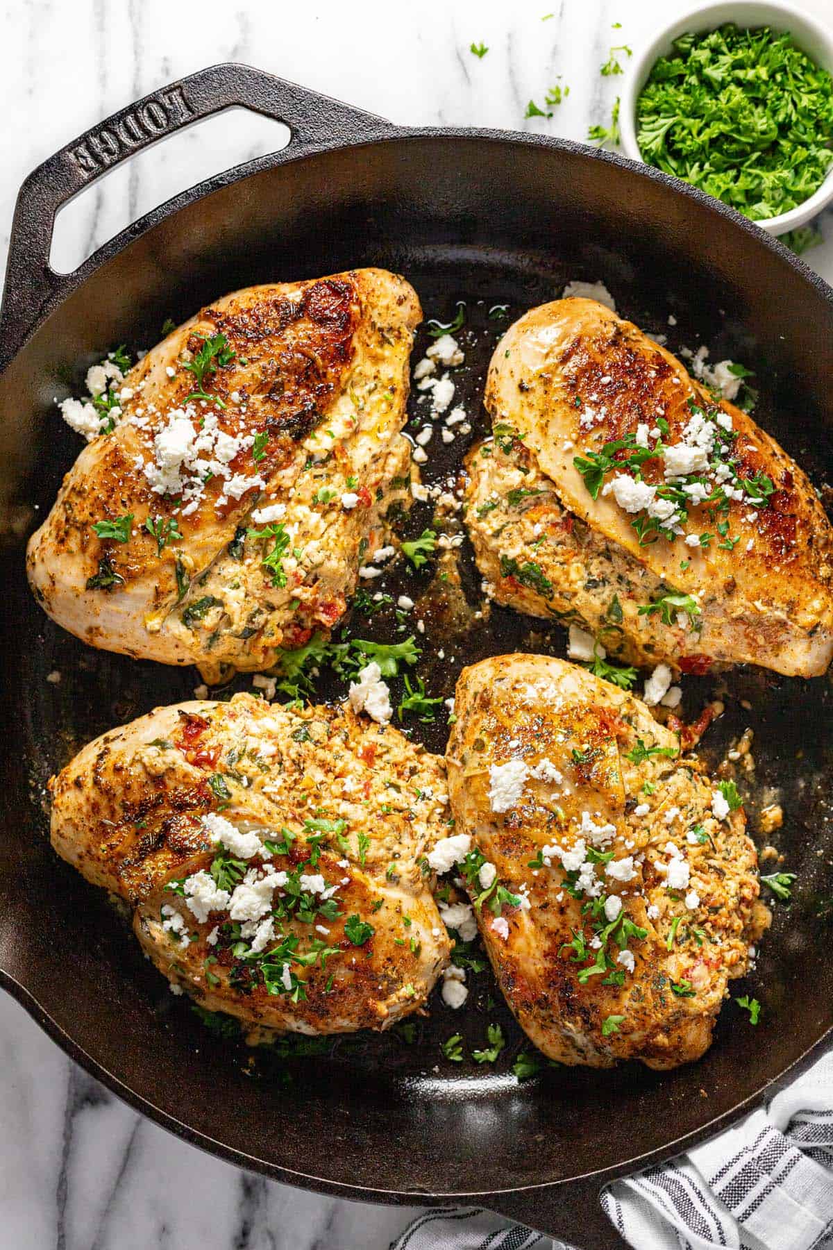 Cast iron skillet with baked stuffed chicken breast topped with feta and parsley. 