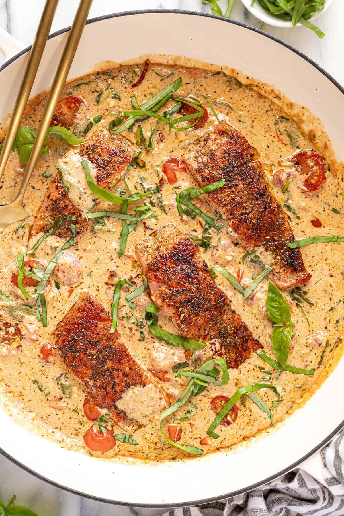Large sauté pan filled with creamy Tuscan salmon garnished with fresh basil. 