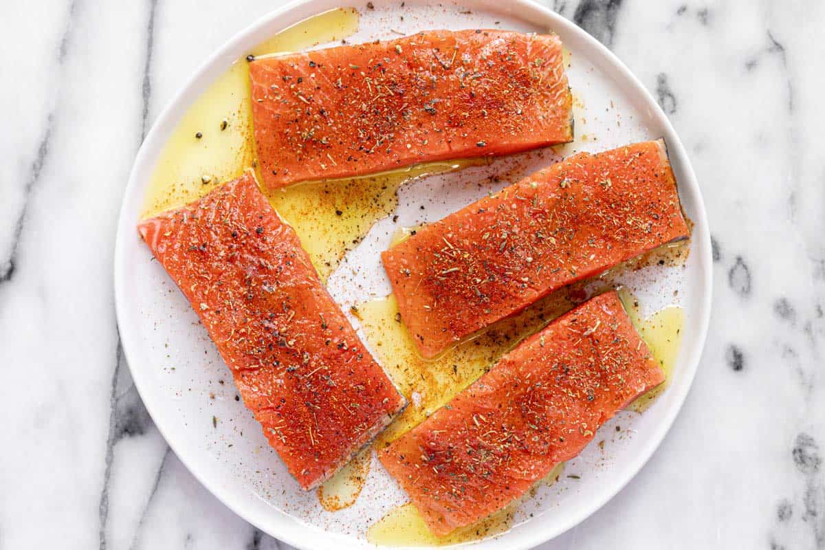 Round plate with salmon seasoned with olive oil, herbs, and spices. 