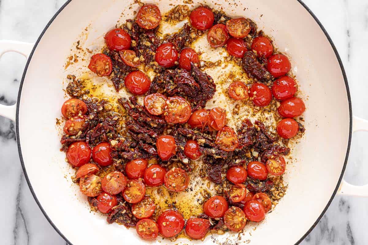 Large sauté pan filled with sauteed garlic, sun-dried tomatoes, and cherry tomatoes. 