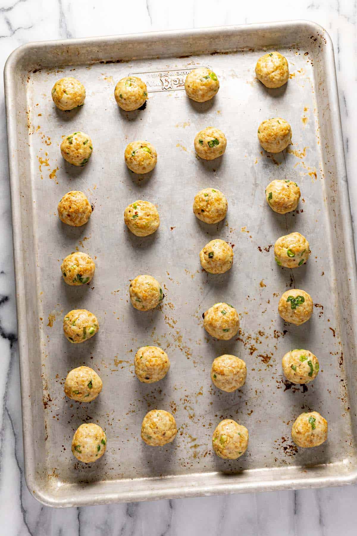 Baked chicken meatballs on a large baking sheet. 