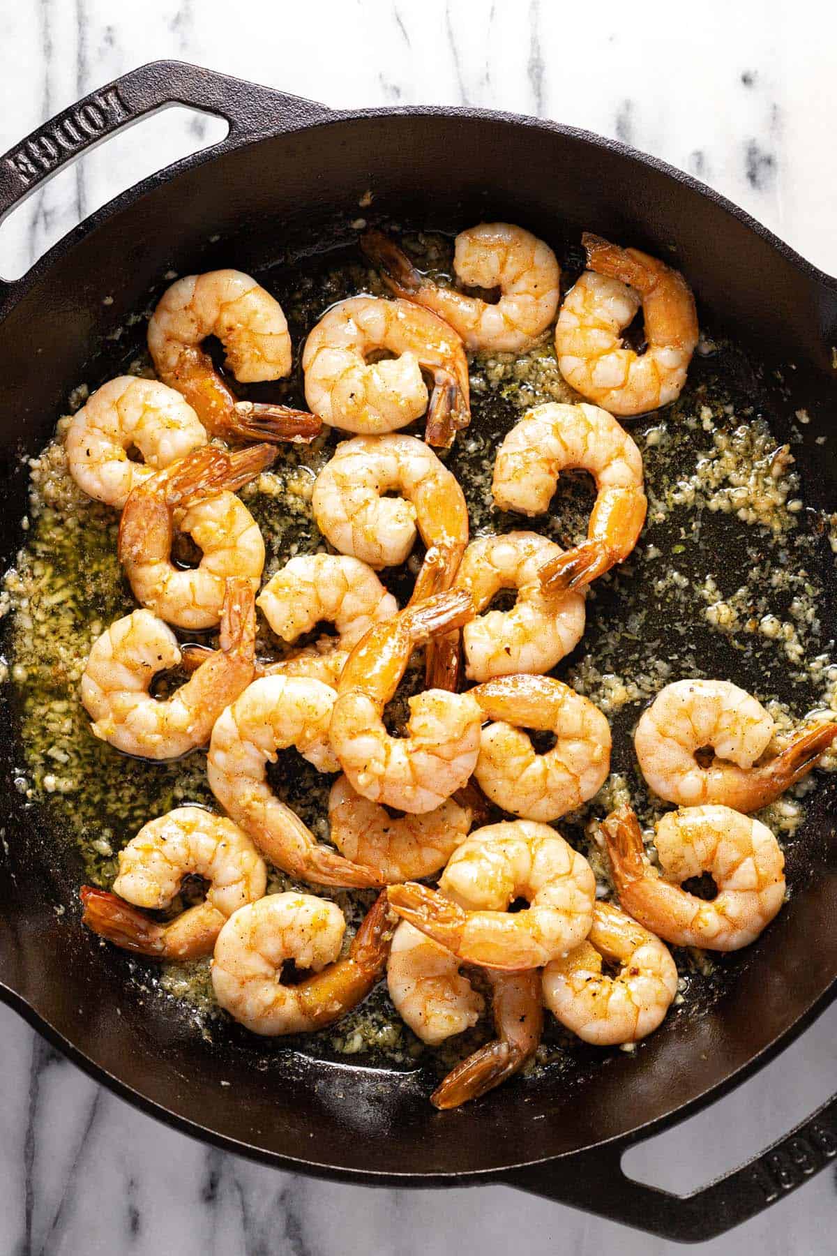 Cast iron pan filled with sauteed shrimp in a garlic butter sauce. 