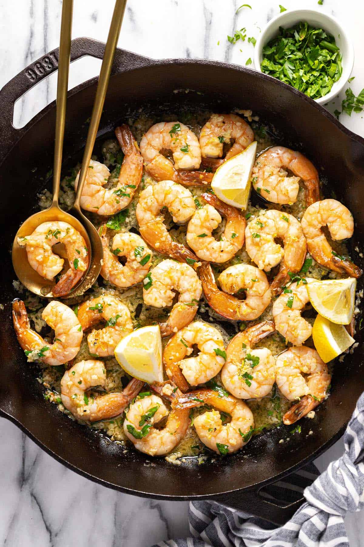 Cast iron pan filled with garlic butter shrimp garnished with lemon wedges.