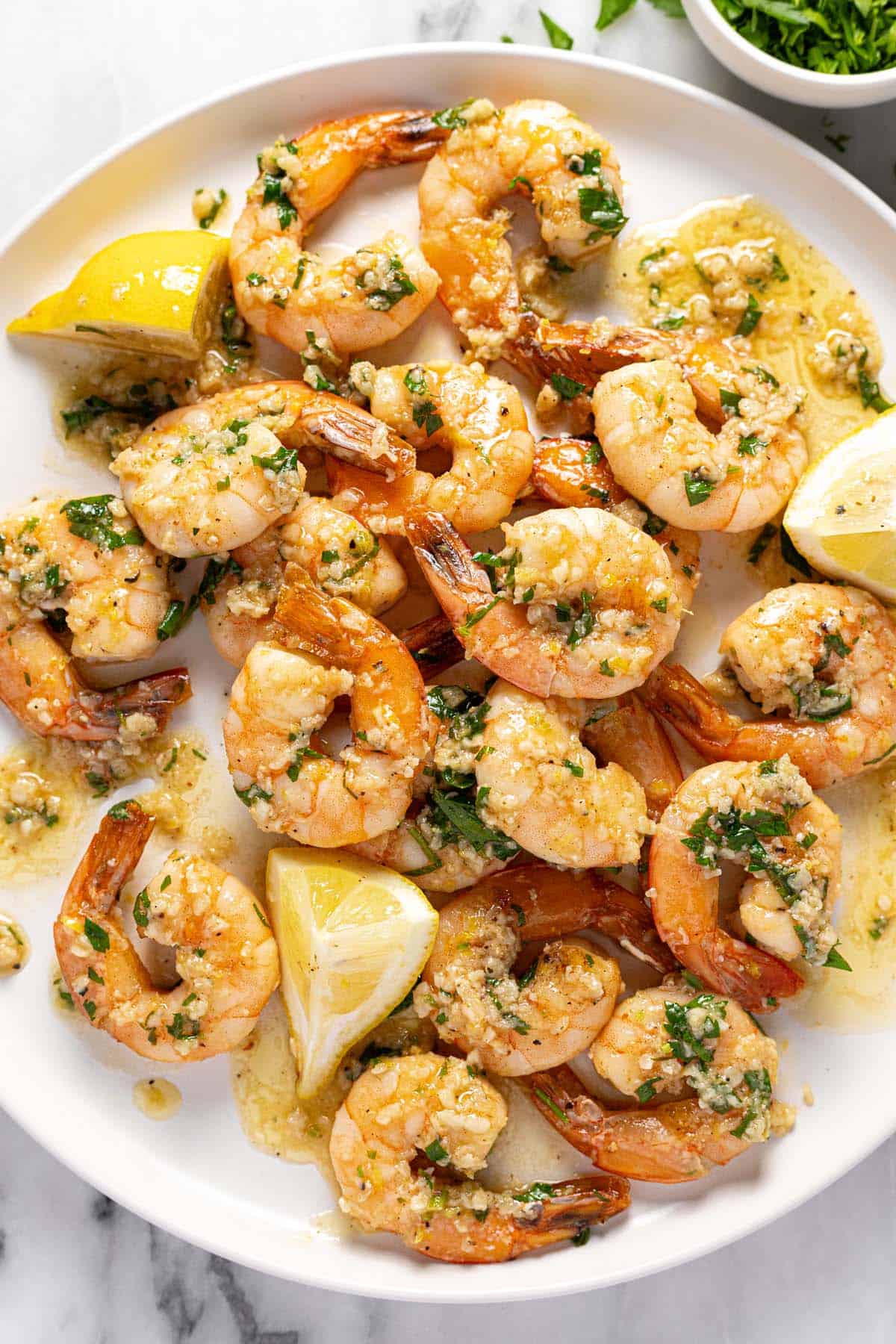 Large round plate piled high with garlic butter shrimp and lemon wedges. 