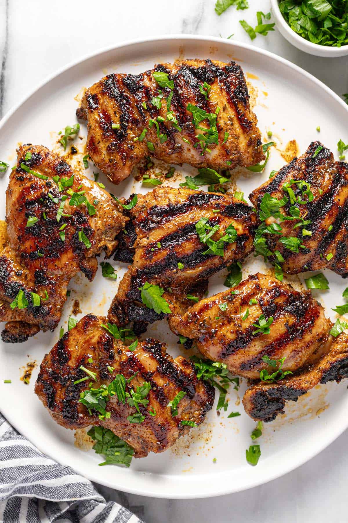 Round plate with 6 grilled chicken thighs garnished with fresh chopped parsley. 