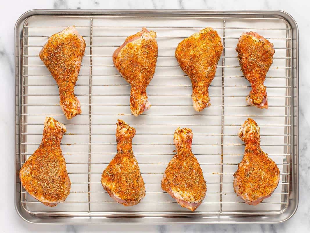 Seasoned chicken legs on a cooling rack on a parchment lined baking sheet. 