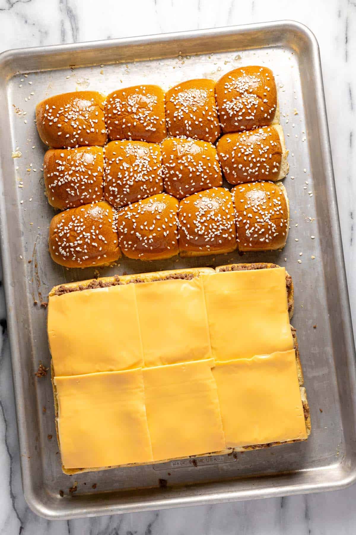 Slider buns topped with sesame seeds and slider buns topped with meat and cheese. 