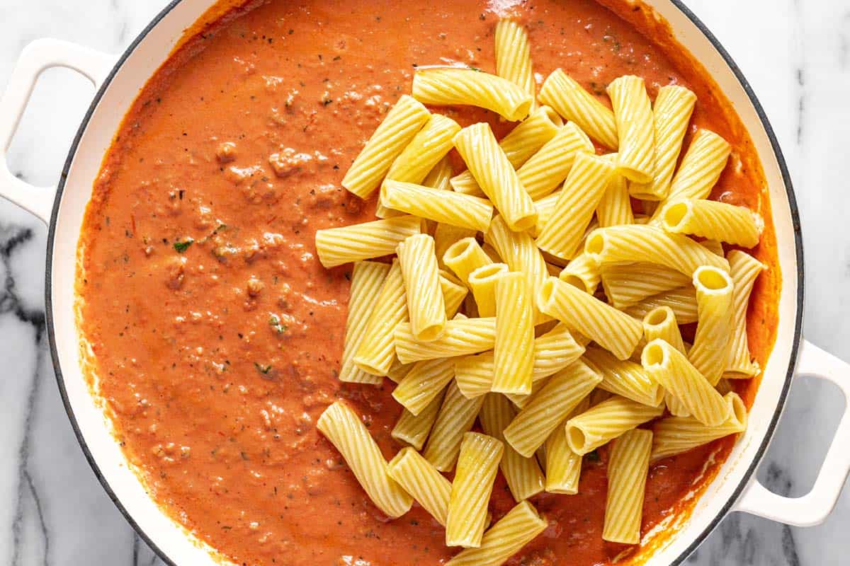 Rigatoni added to a large pan of creamy Italian sausage pasta. 