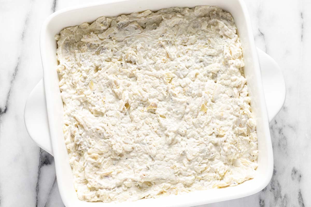 Homemade artichoke dip spread in an even layer in a baking dish.