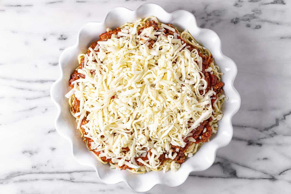 Large pie pan filled with spaghetti and meat sauce topped with cheese. 