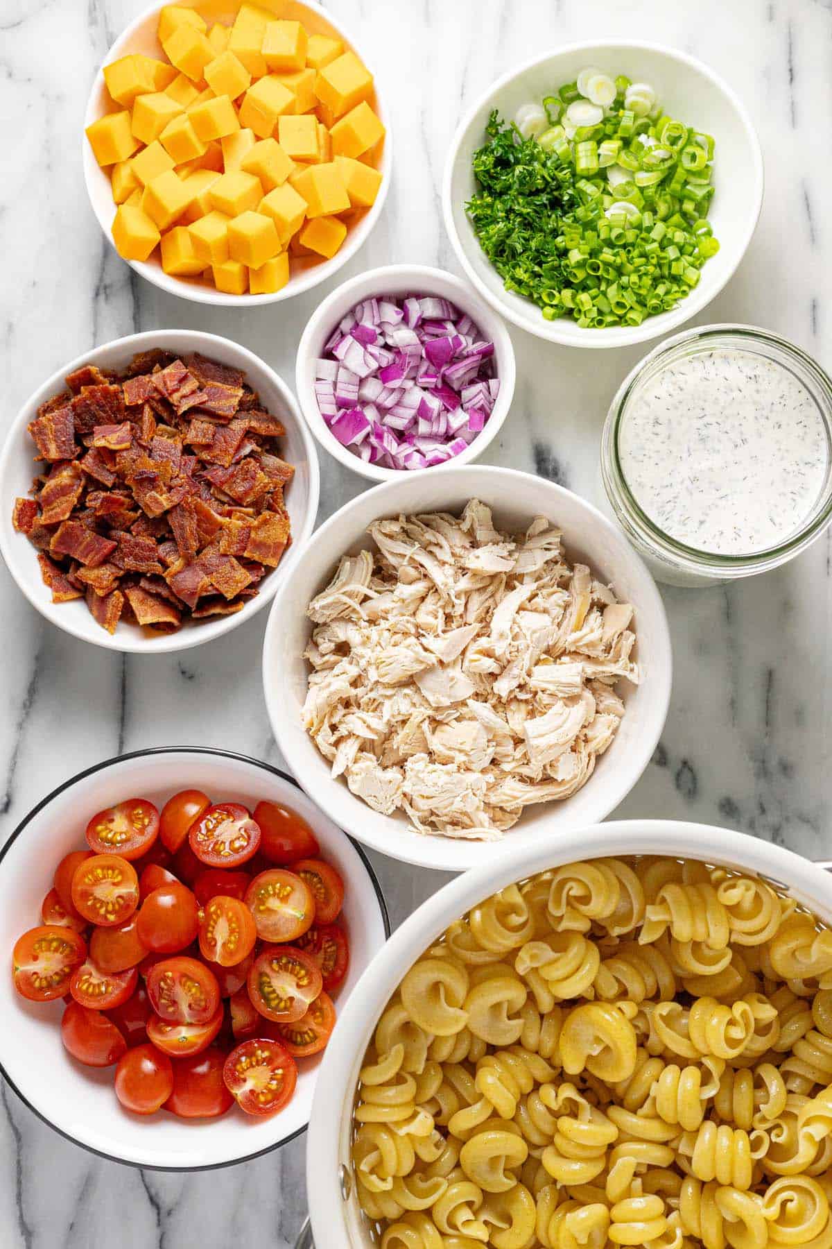 Bowls of ingredients to make chicken ranch pasta salad. 