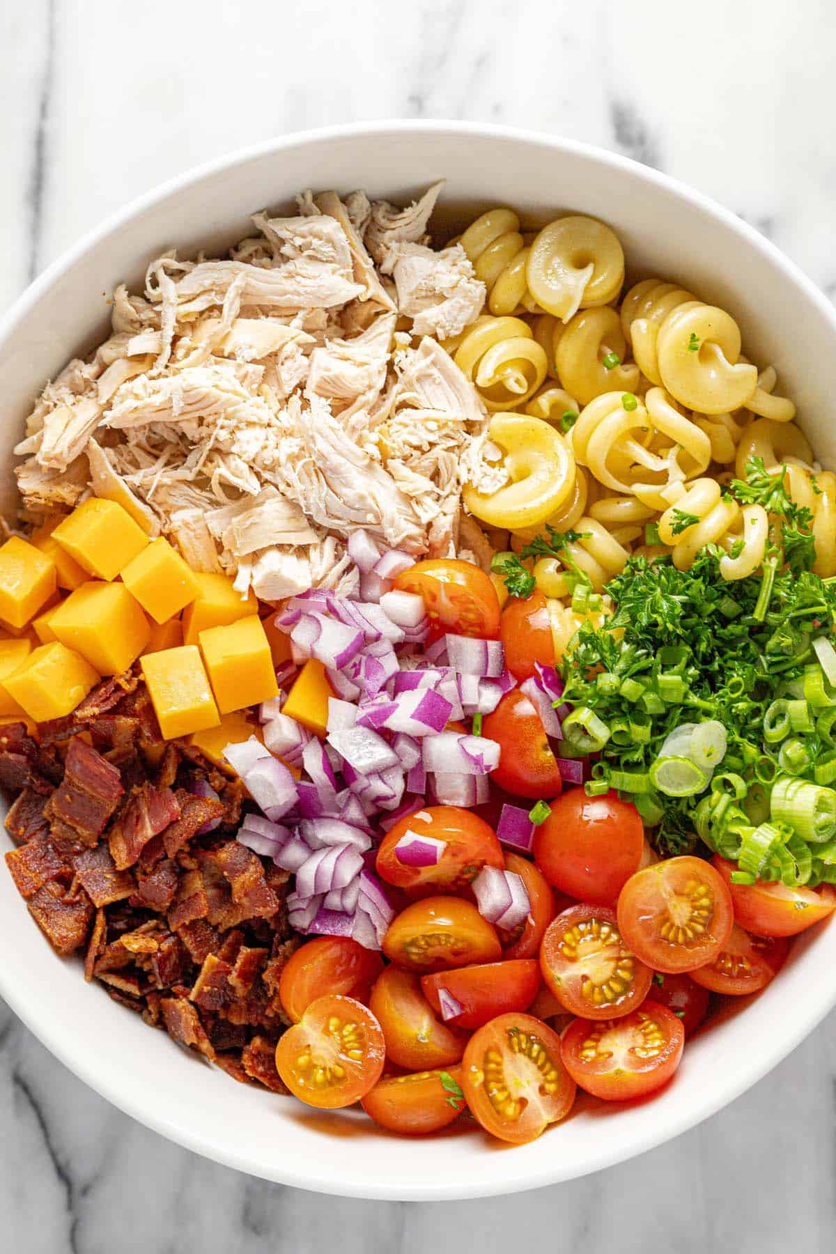 Bowl filled with ingredients to make chicken pasta salad. 