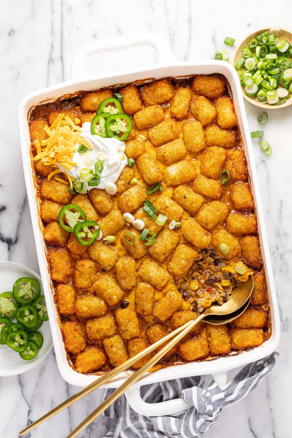 Large baking dish filled with cowboy casserole garnished with sour cream, cheese, and green onion. 