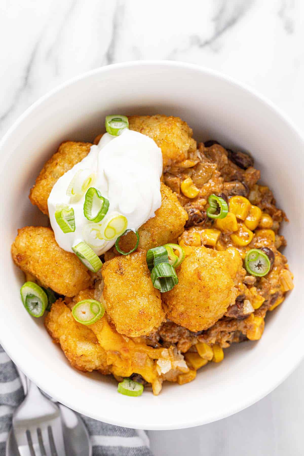 Bowl of cowboy casserole topped with sour cream and green onions. 