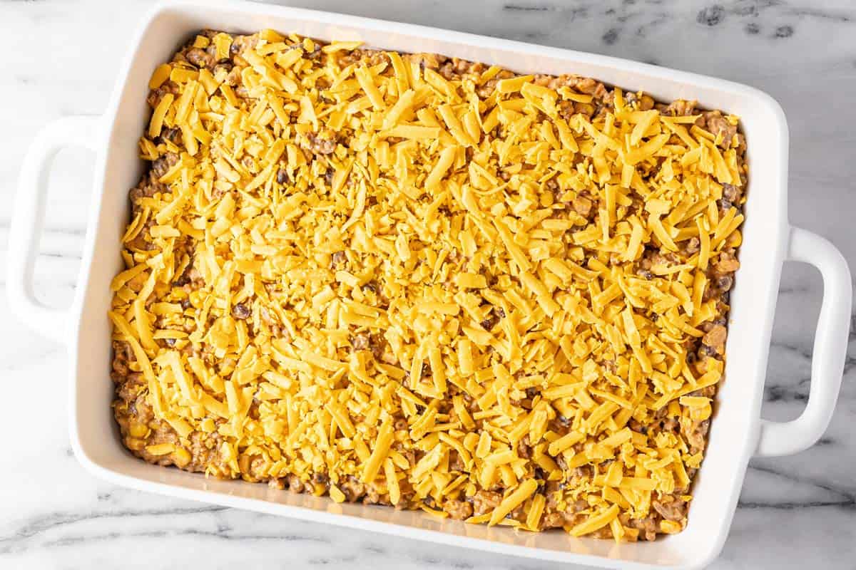 Large white baking dish filled with cowboy casserole topped with shredded cheese. 