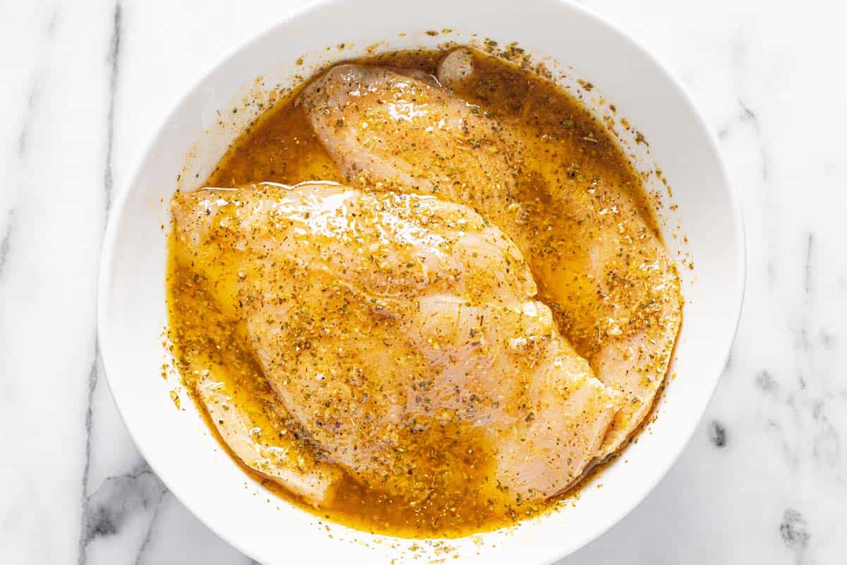 Large bowl filled with marinating Greek chicken. 