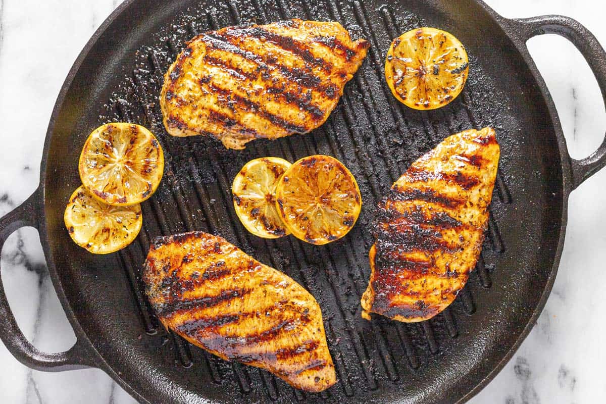 Round grill pan with grilled Greek chicken and lemon slices. 