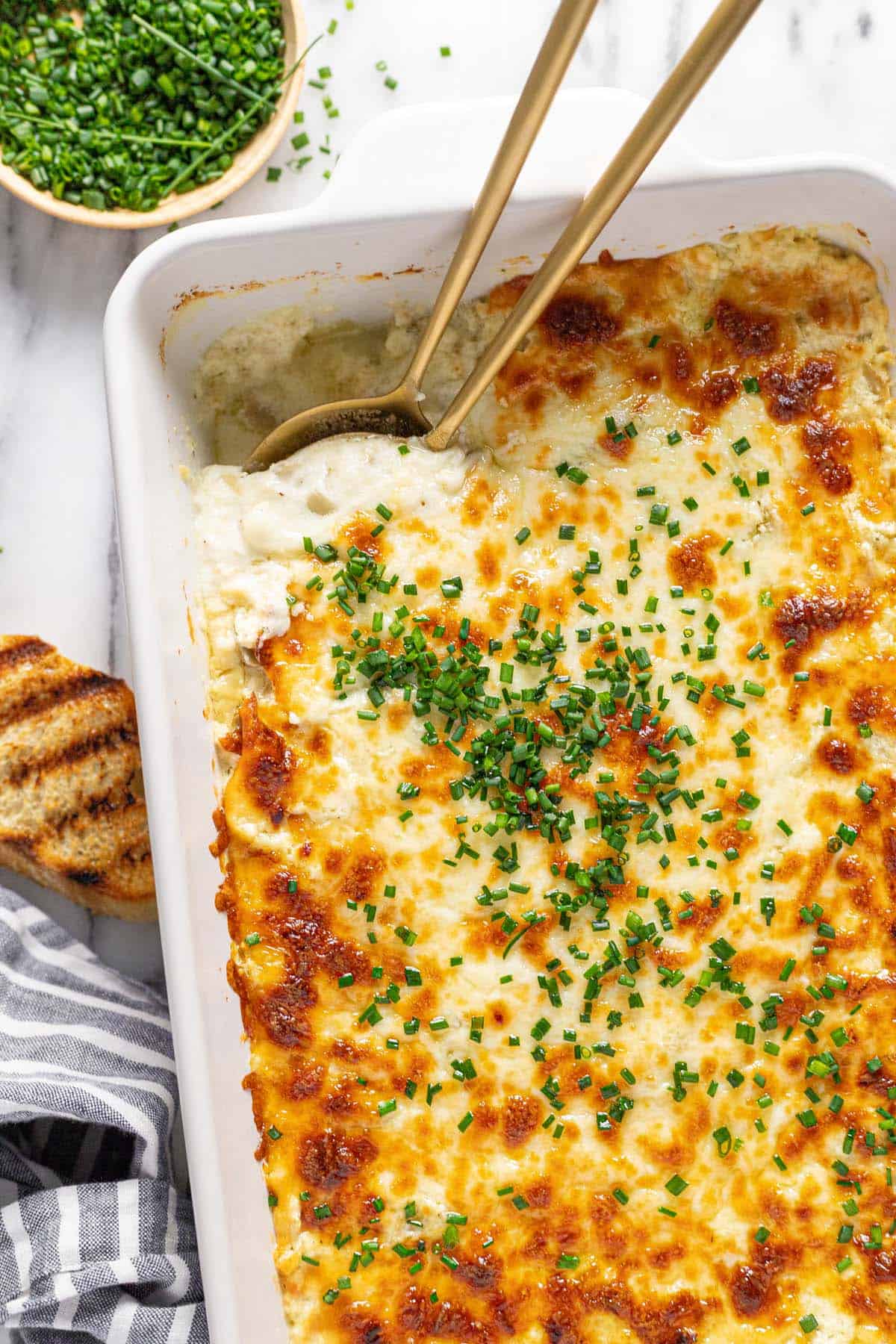 Close up shot of creamy feta dip garnished with chives in a large baking dish. 