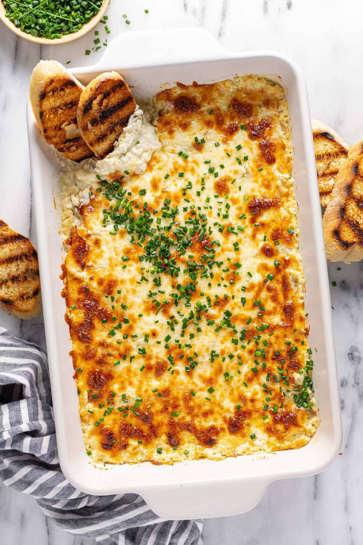 Large baking dish filled with creamy artichoke and feta dip garnished with chives. 