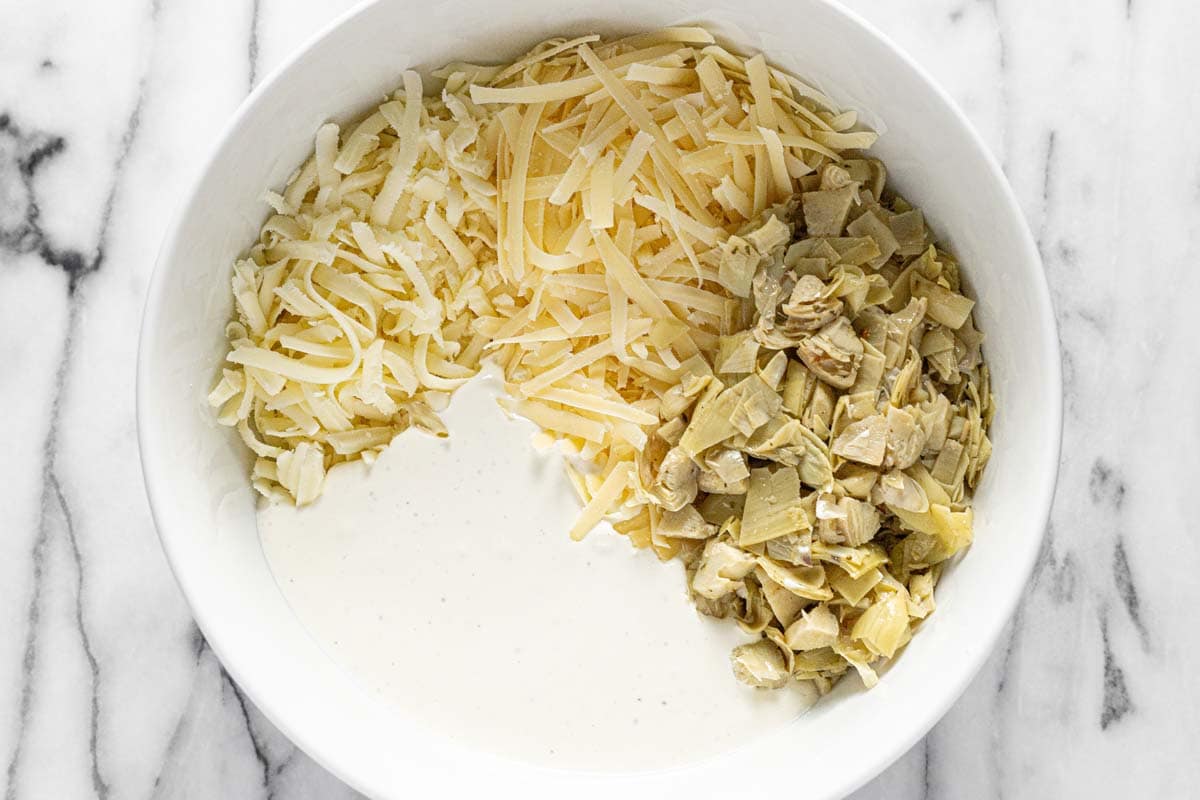 Bowl filled with ingredients to make baked artichoke and feta dip. 