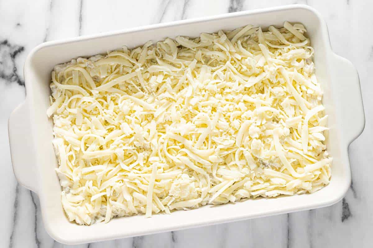 Creamy feta dip in a baking dish with shredded mozzarella cheese on top. 