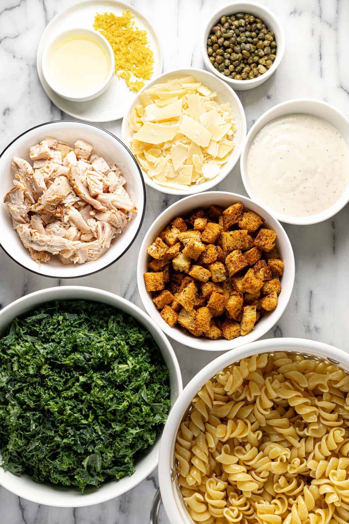 Bowls of ingredients to make chicken Caesar pasta salad. 