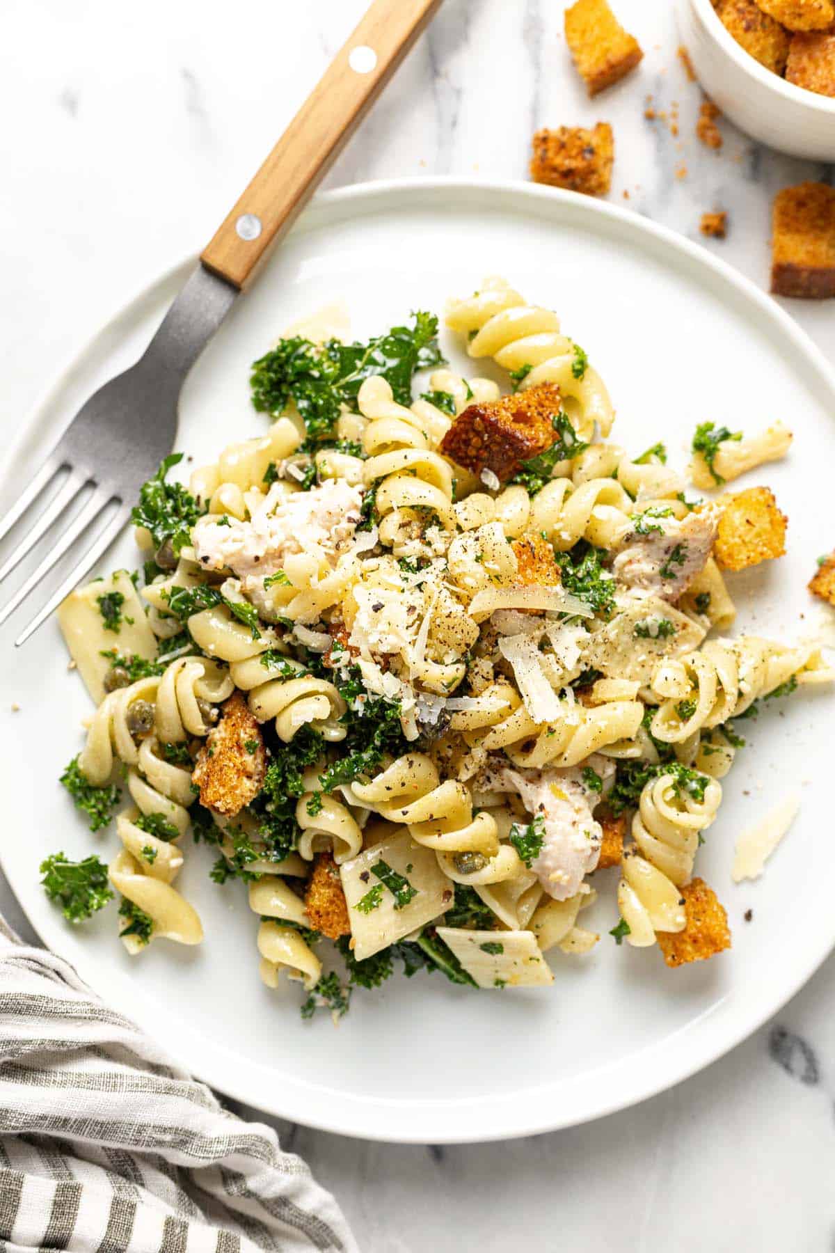 Plate with chicken Caesar pasta salad topped with Parmesan cheese. 